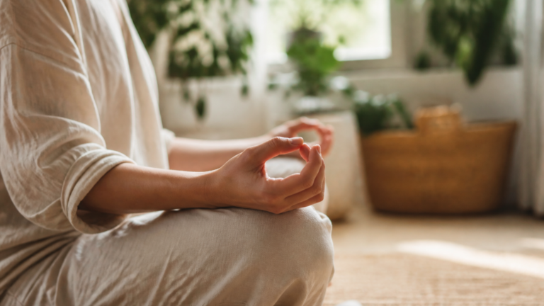Personne en posture de méditation dans un intérieur calme et lumineux, mains posées sur les genoux, ambiance douce et apaisante