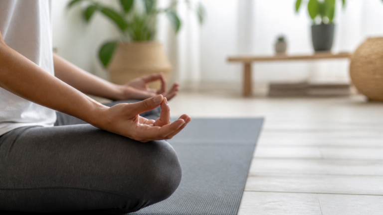 Personne méditant tranquillement dans un intérieur lumineux et apaisant, mains posées sur les genoux en position de méditation